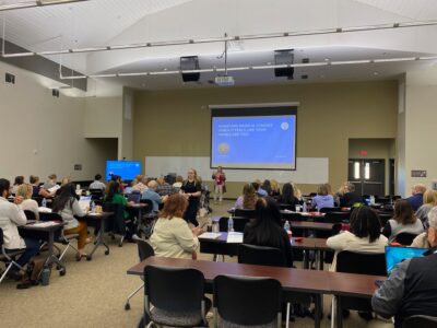 Room full of simulationists watching a presentation while sitting at long tables